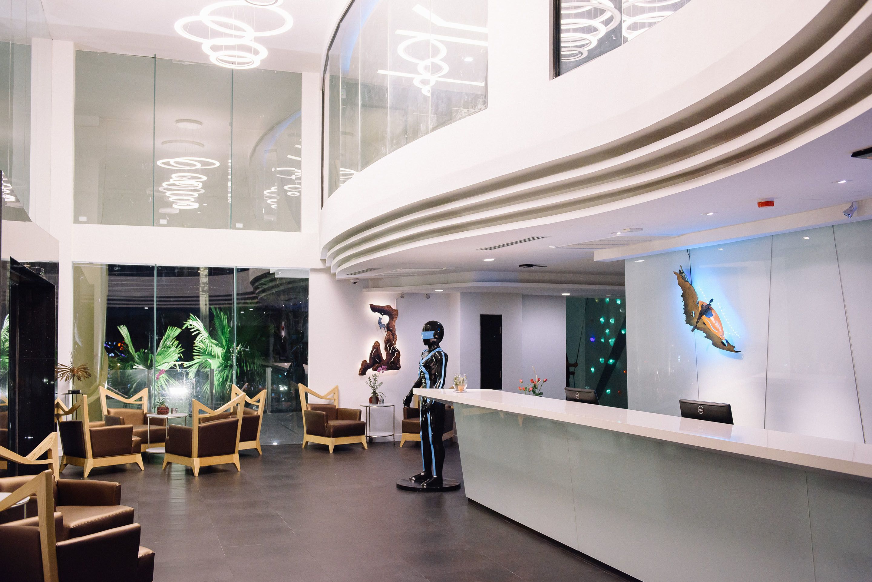 A modern hotel lobby with a curved reception desk, seating area with brown chairs, and a large window offering a view of the night sky.