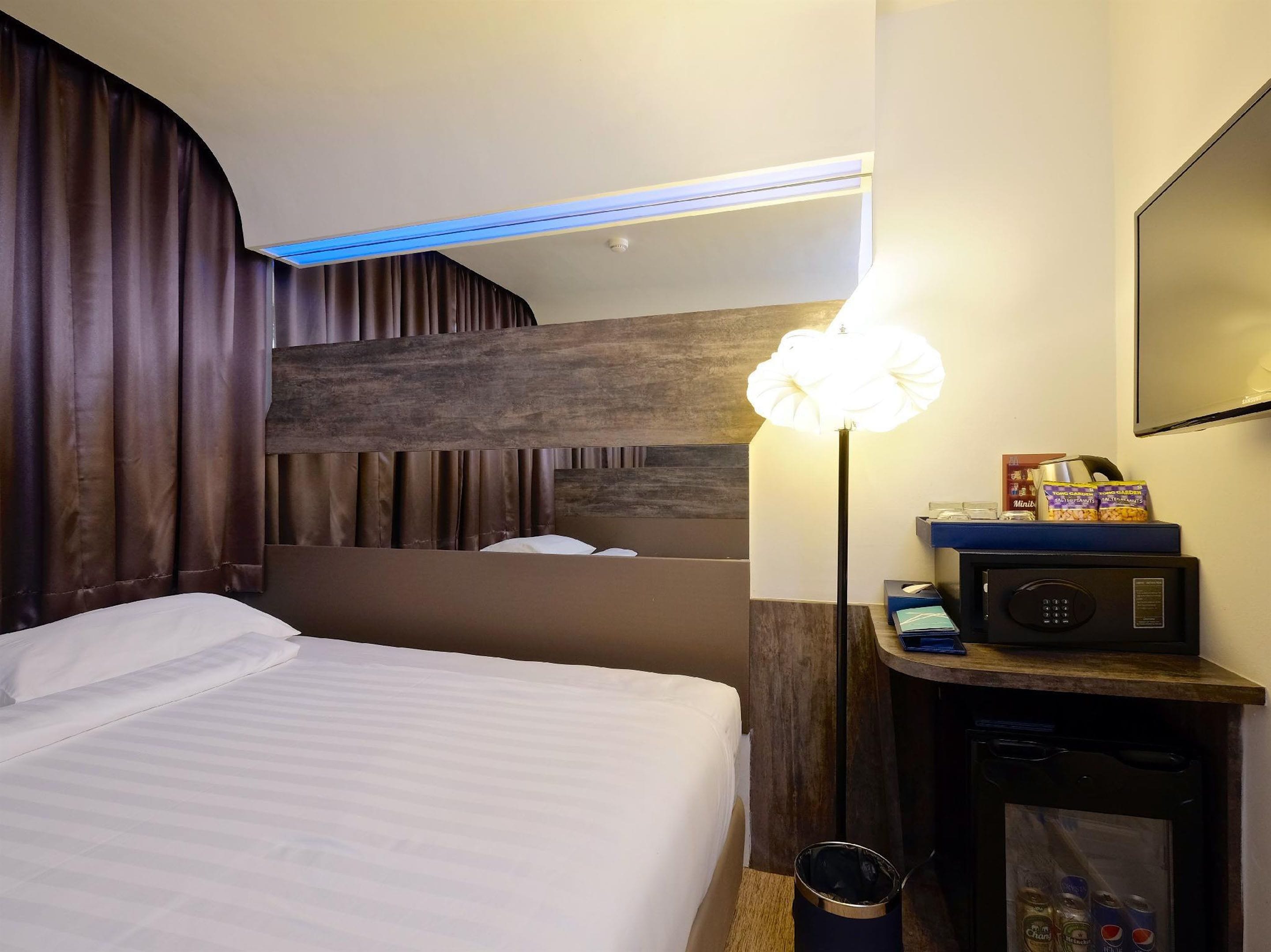 A hotel room with a bed, a bedside lamp, a microwave, and a minibar.