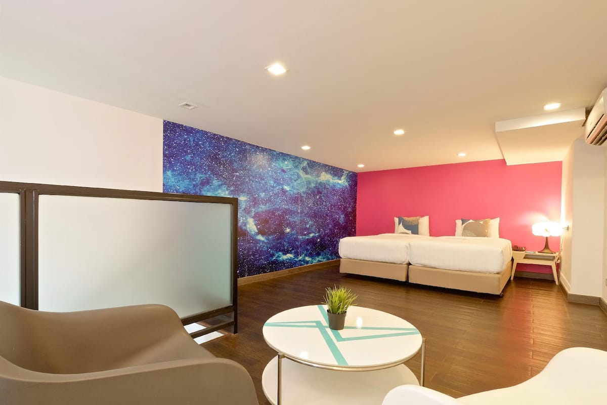 A modern hotel room with a galaxy-themed wall, a sofa bed, a small round table with a plant, and a large window.