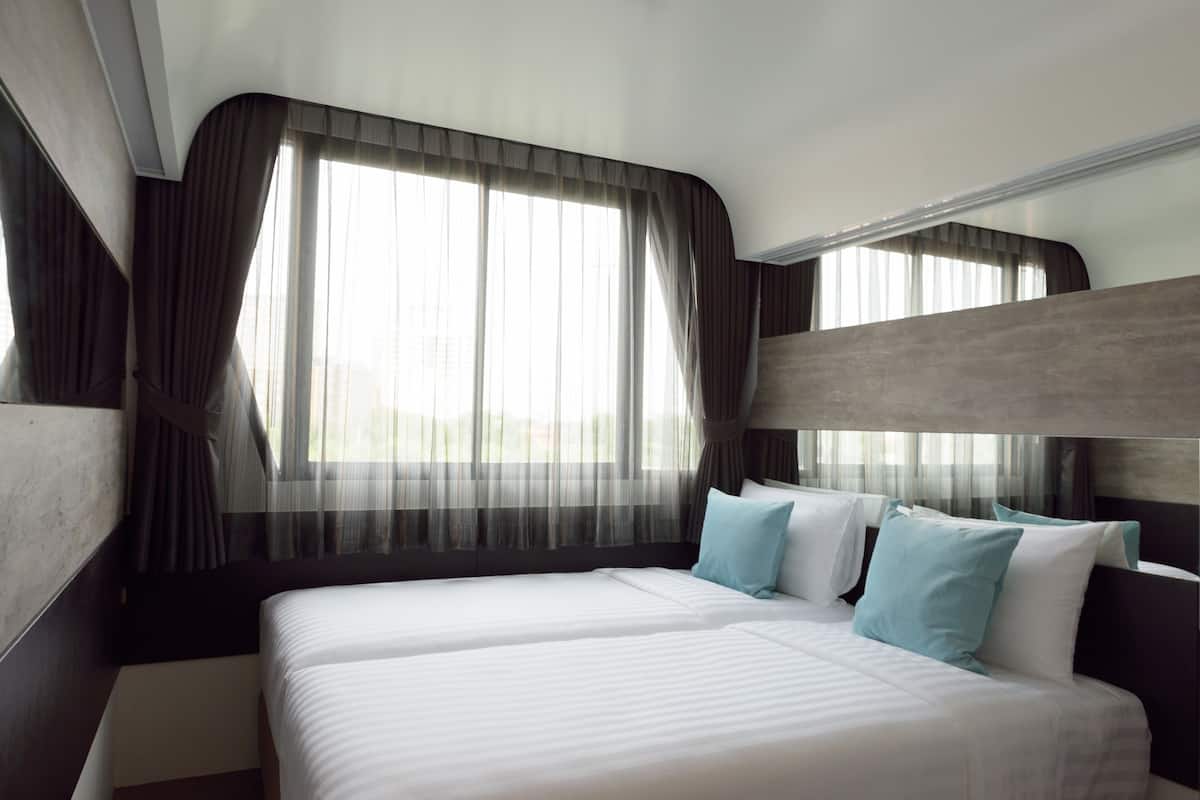 A hotel room with two beds, a large window with sheer curtains, and a modern design.