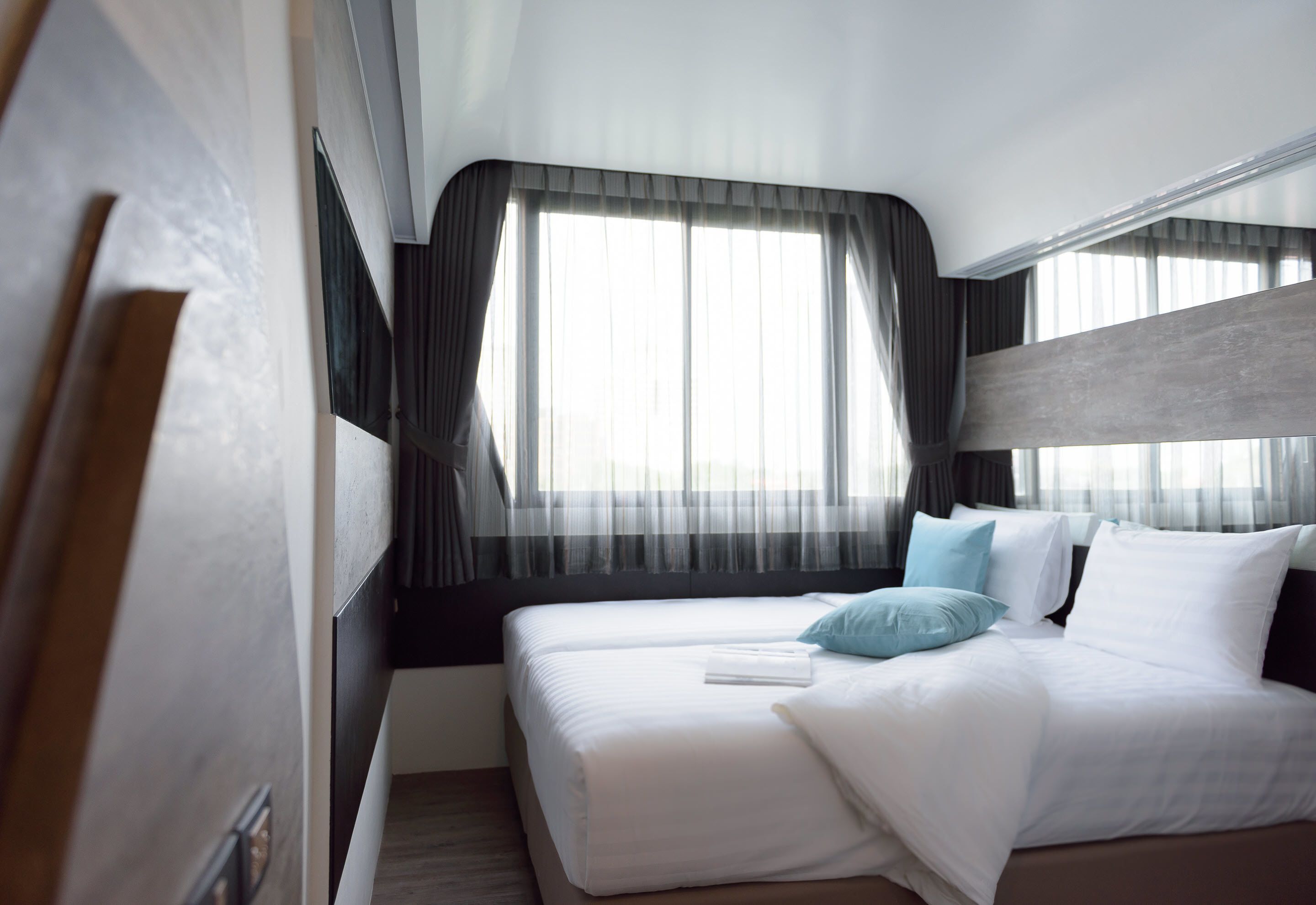 A hotel room with two beds, a large window with sheer curtains, and a modern design.