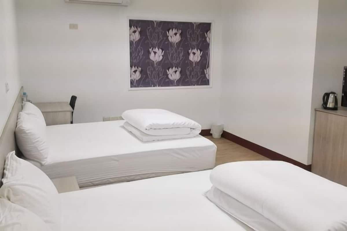 A hotel room with two beds, a small desk, a chair, and a wall-mounted air conditioner.