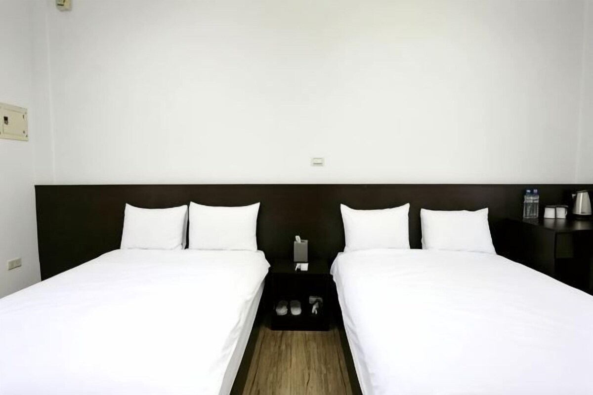 A double bed with white linens, a dark headboard, and a small bedside table with a lamp.