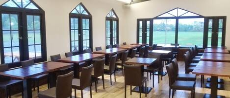 Amplia habitación con grandes ventanales, mesas y sillas de madera dispuestas para comer.