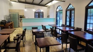 Un restaurant avec des tables et des chaises en bois, un espace cuisine et de grandes fenêtres.