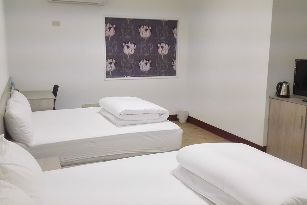 A hotel room with two beds, a television, a small table, and a window with a floral curtain.