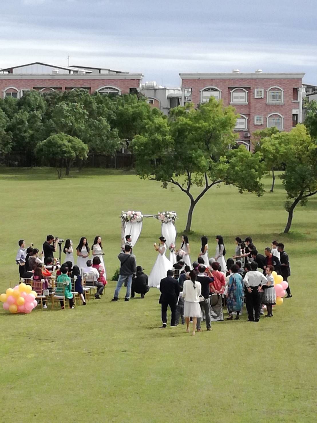 A wedding ceremony in an open field with a building in the background.