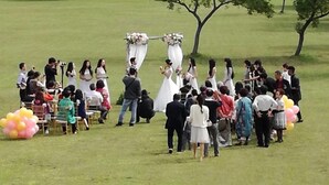 Une cérémonie de mariage qui se déroule dans un champ en plein air, avec un bâtiment en arrière-plan.