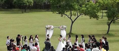 A wedding ceremony in an open field with a building in the background.