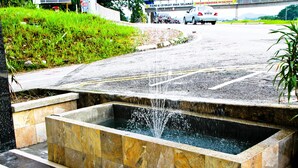 A rectangular water feature with a fountain in the center, surrounded by stone tiles.