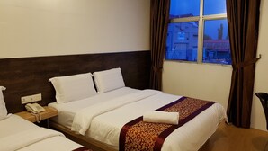 A hotel room with two beds, a wooden headboard, a bedside telephone, and a window with curtains.