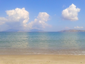 A beach with clear water, a sandy shore, and distant mountains under a blue sky with clouds. - Anthia Apartments (Kos)