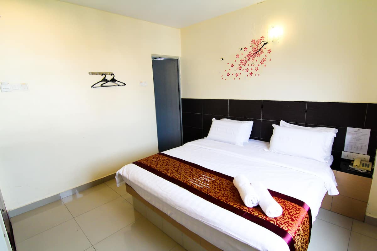A neatly made bed with white linens and a brown decorative runner, a wall-mounted light fixture, and a door to the left.