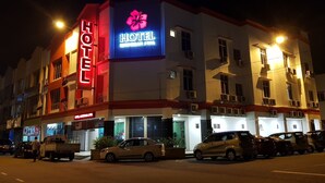 A hotel building with a prominent neon sign, multiple air conditioning units, and a parking lot with several cars.