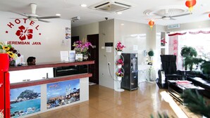 A hotel reception area with a reception desk, a refrigerator, a black leather sofa, and a ceiling fan.