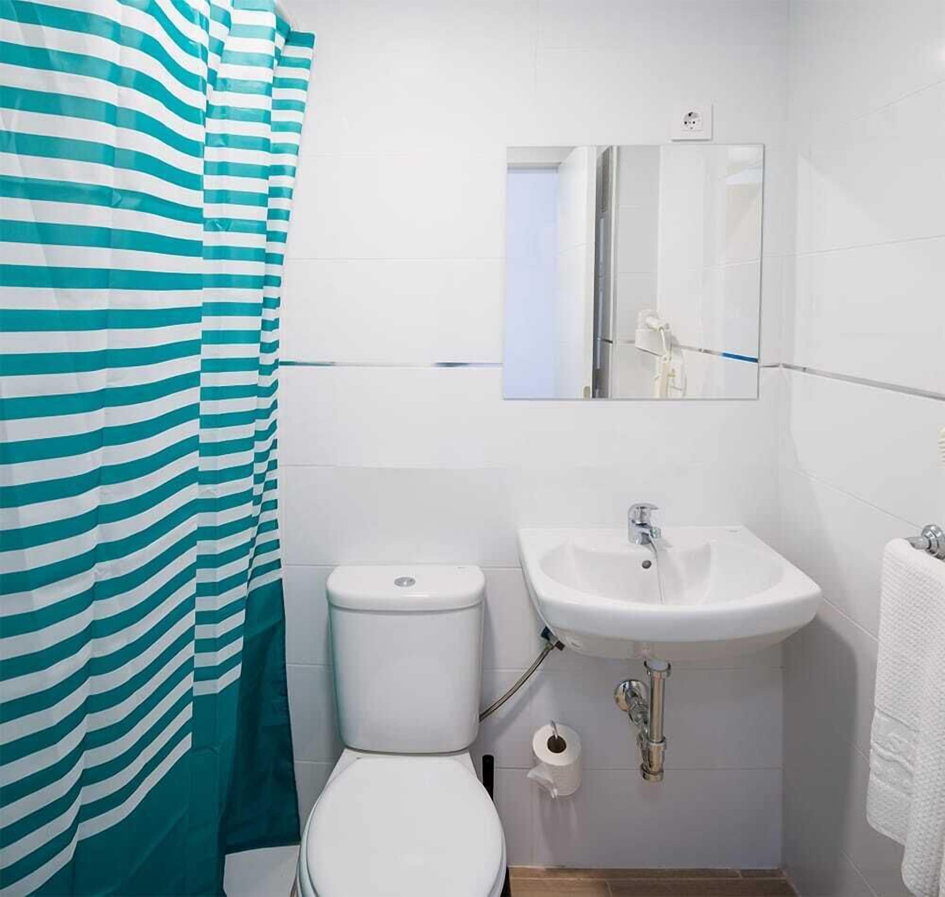 Ein Badezimmer mit gestreiftem Duschvorhang, einer weißen Toilette, einem Waschbecken mit Spiegel und einem Handtuch an der Wand.