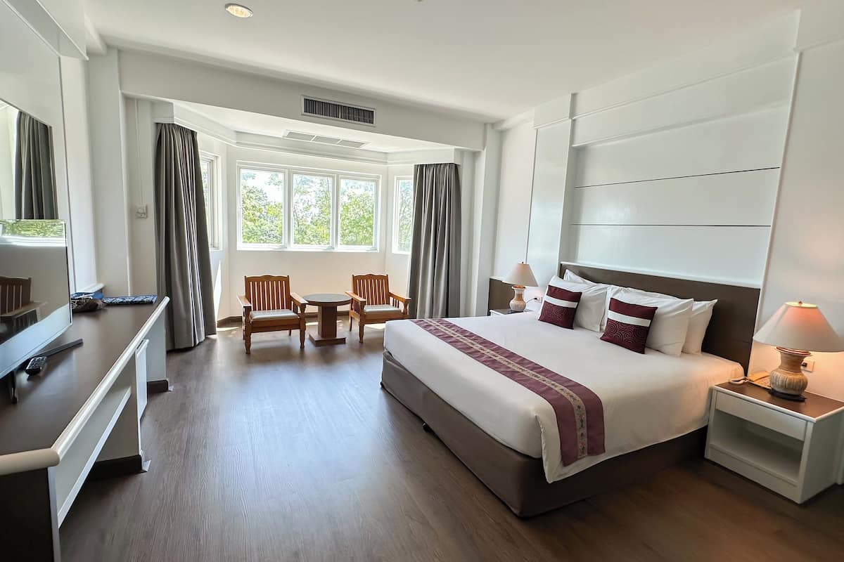 Una habitación de hotel con una cama grande, un escritorio con televisor, una silla, una mesita y una lámpara.
