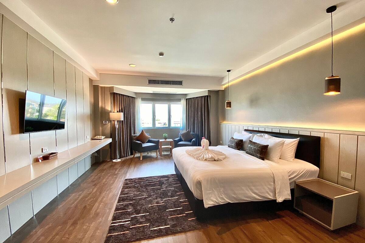 Una habitación de hotel moderna con una cama grande, un televisor montado en la pared, un escritorio y un área de estar con una mesa y sillas.