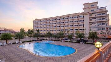A hotel with a swimming pool, palm trees, and a large building with multiple floors.