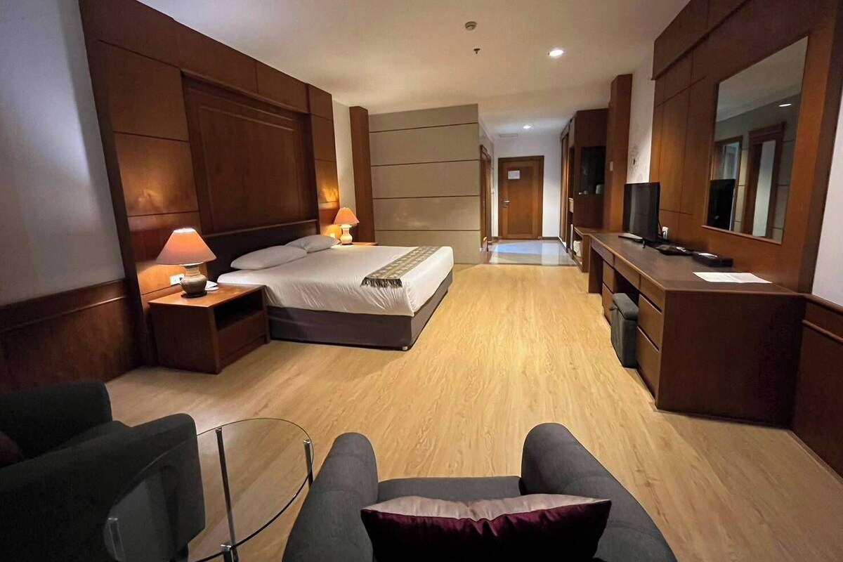 A hotel room with a bed, bedside lamps, a desk with a computer, a chair, and a TV.