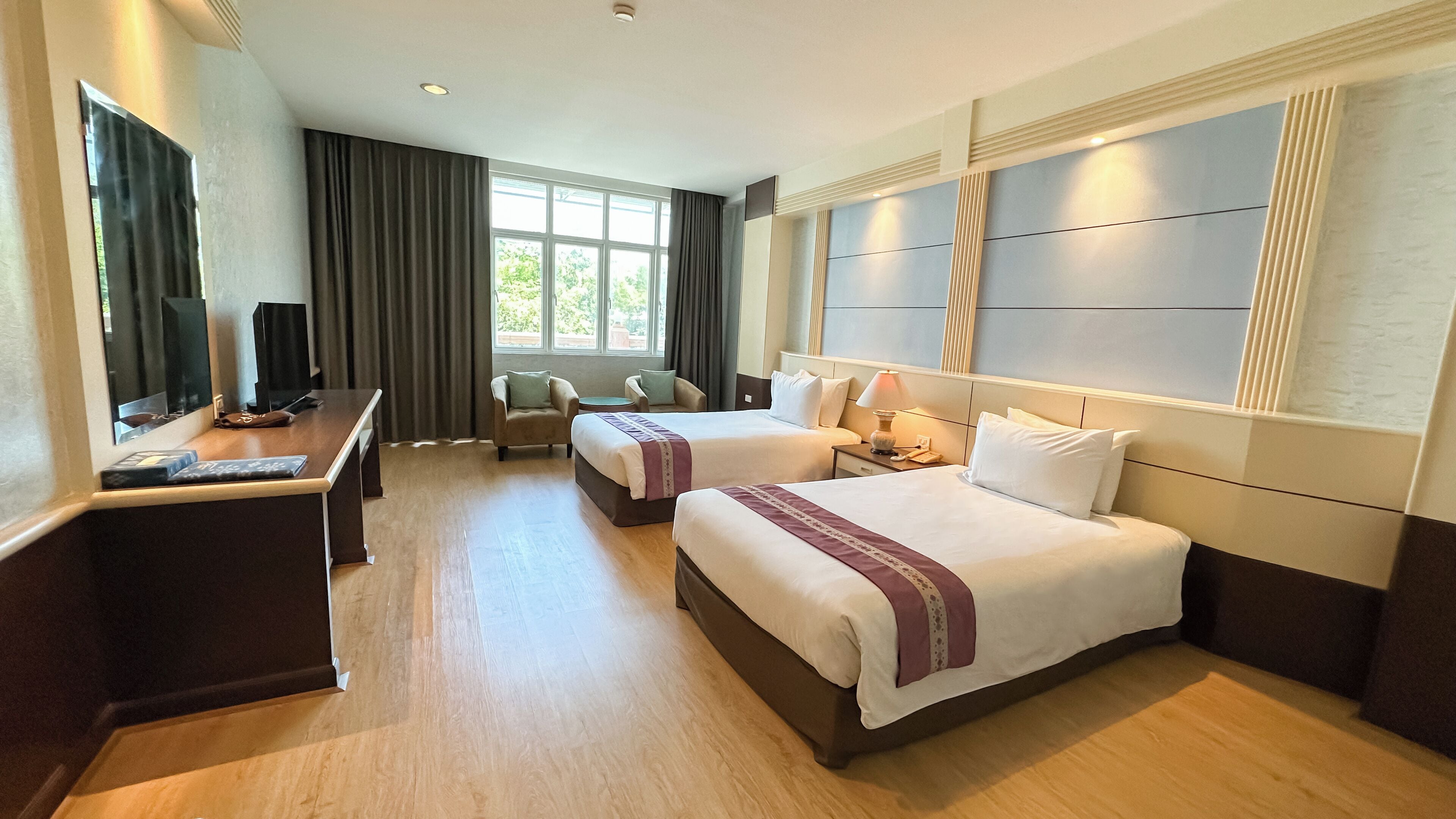 A hotel room with two beds, a desk, a chair, a TV, and a window with curtains.