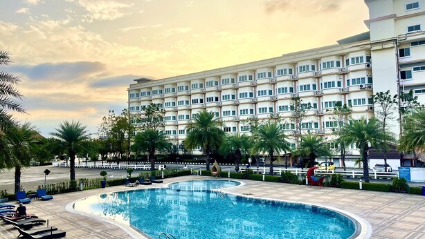 Un hotel con piscina, sillas de descanso y palmeras.