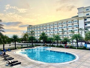 Et hotel med swimmingpool, liggestole og palmer.