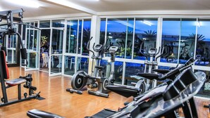 Un gimnasio con máquinas de cardio, equipo de levantamiento de pesas y amplias ventanas que ofrecen vista a una piscina y zona exterior.