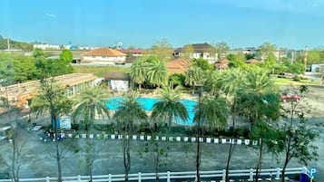 A view of a residential area with a swimming pool surrounded by palm trees, a parking lot, and houses in the background.