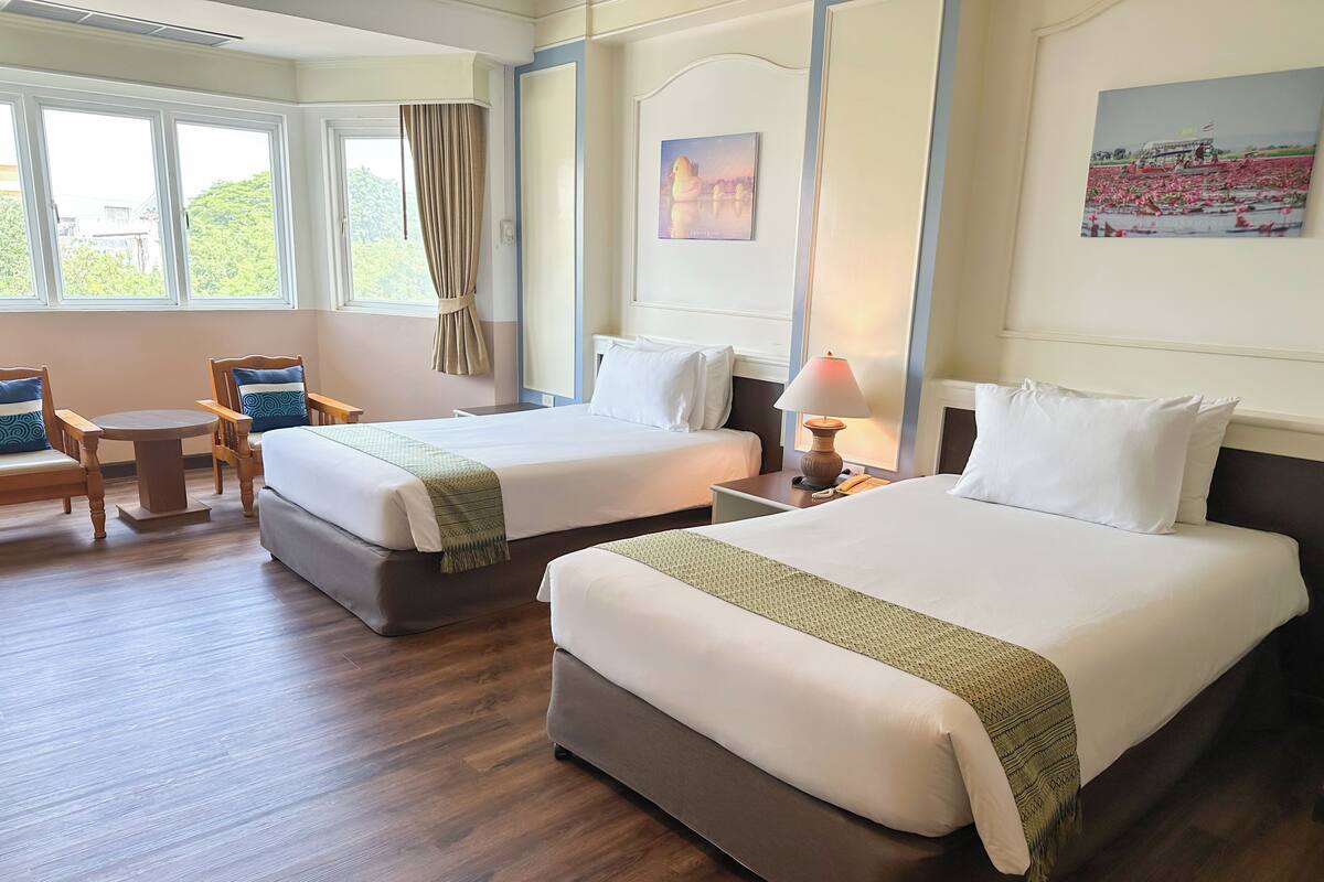 Una habitación de hotel con dos camas, una mesita, sillas y un ventanal con cortinas.