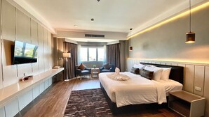 Una habitación de hotel moderna con una cama grande, un televisor montado en la pared, un escritorio y una zona de estar con una mesa y sillas.