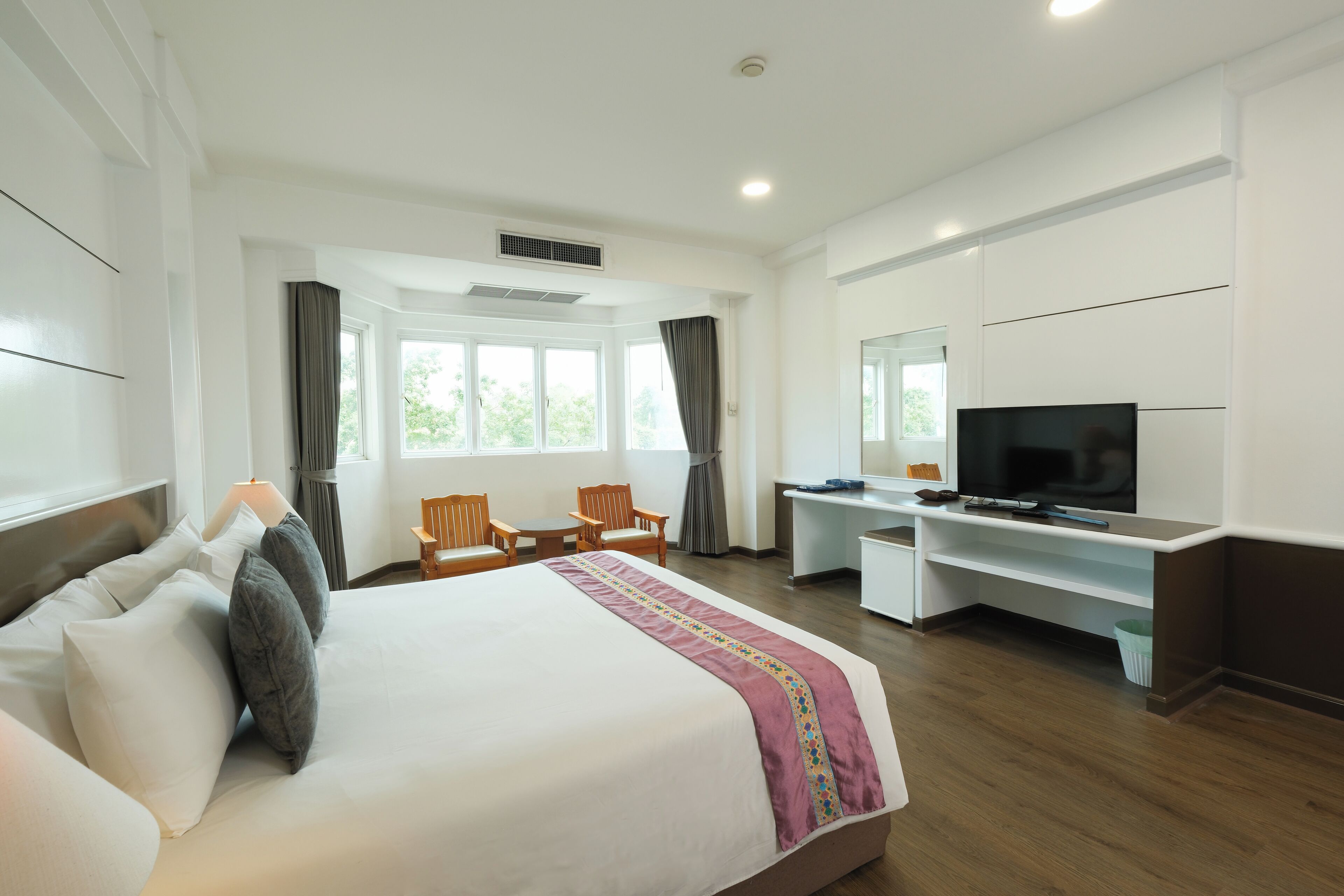 A hotel room with a large bed, a desk with a TV, two chairs, and a window with curtains.