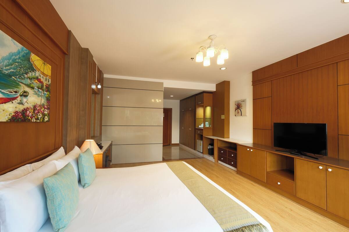Una habitación de hotel moderna con una cama grande, armarios de madera, un televisor y un cuadro en la pared.