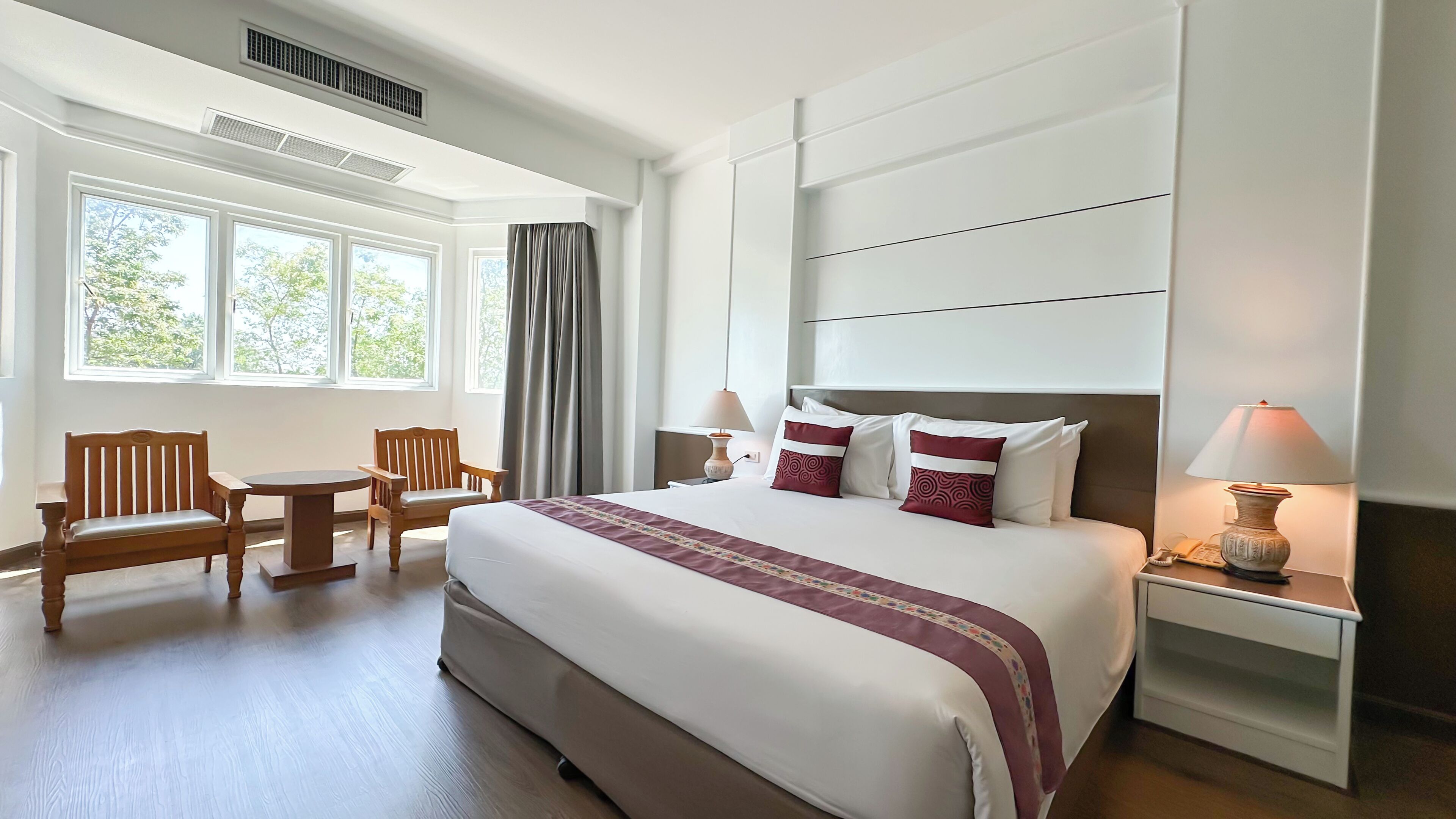 Habitación de hotel con una cama grande, dos mesitas de noche, una silla, una mesita pequeña y una ventana con cortinas.
