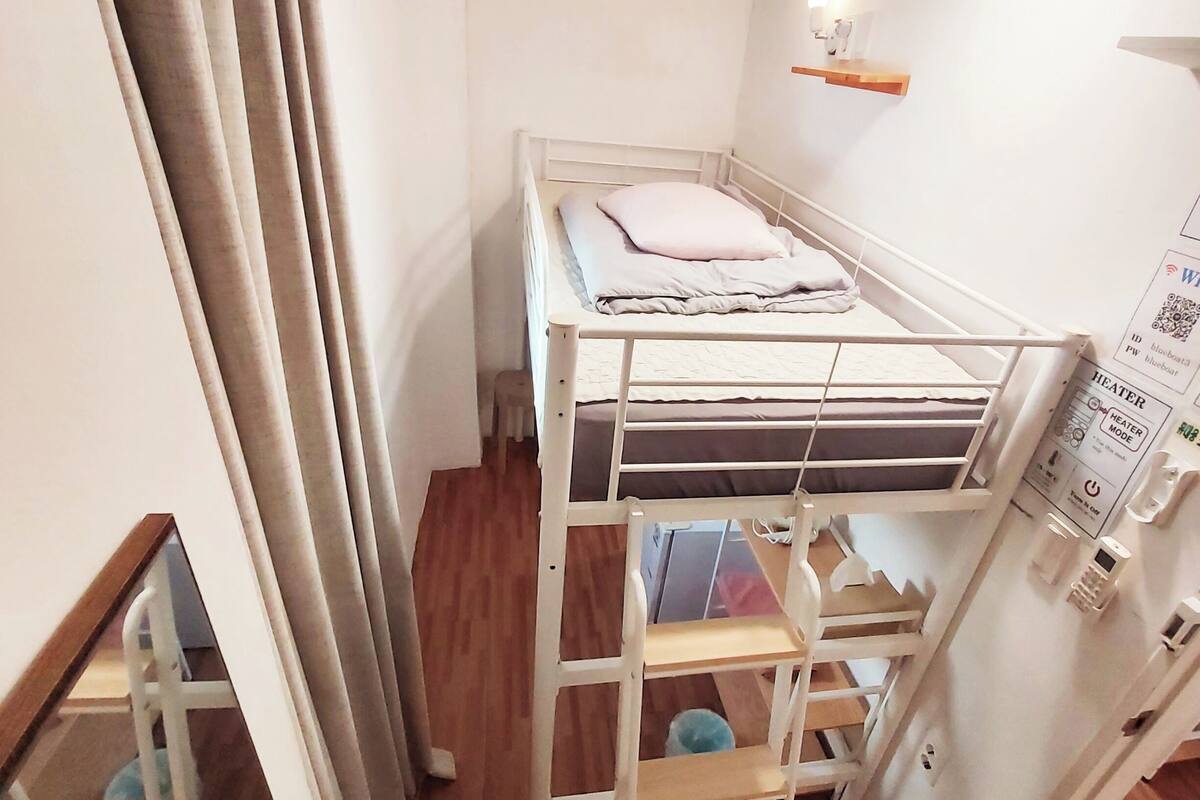 A compact room with a bunk bed, a small ladder, a heater, and a shelf.