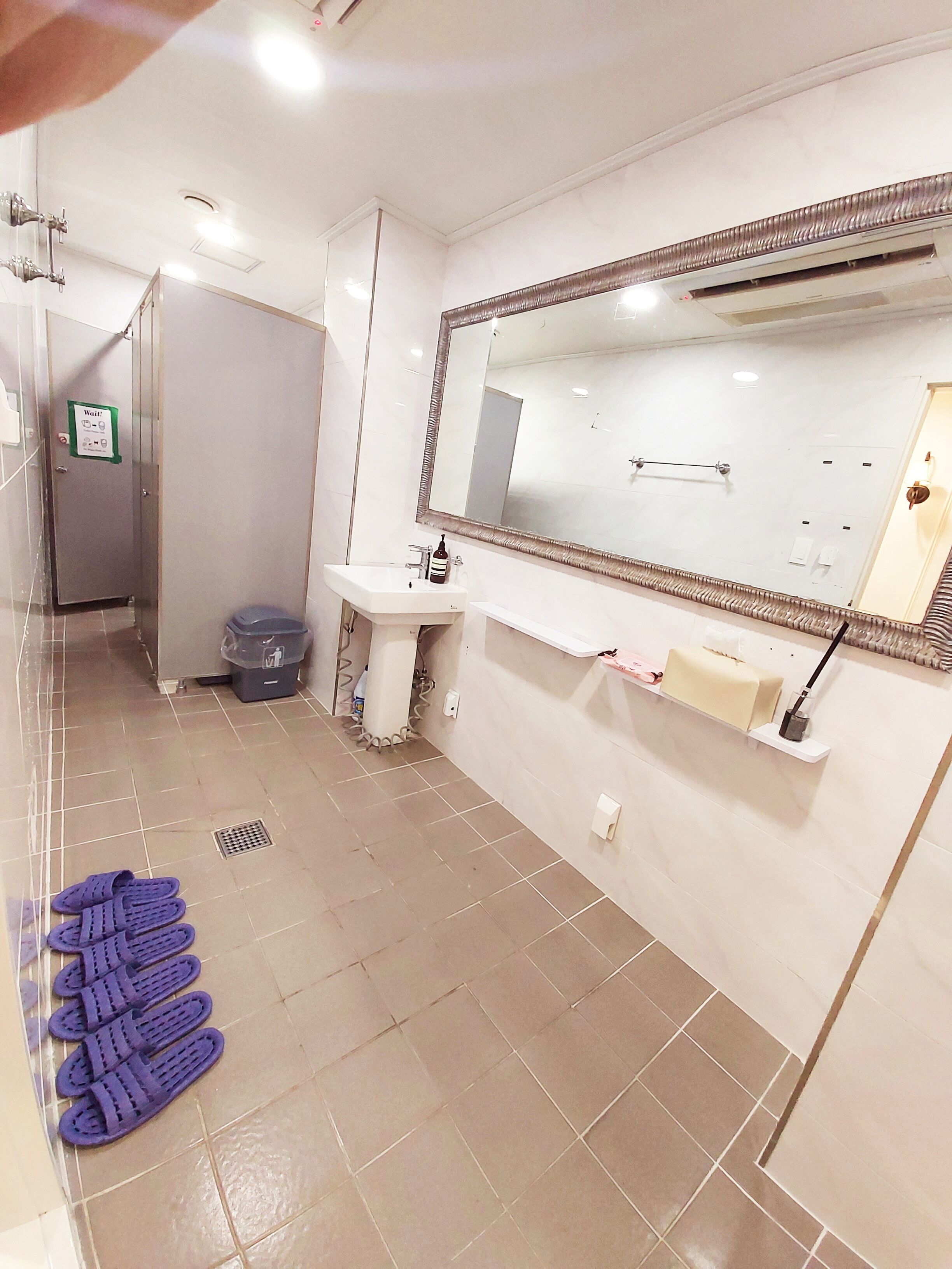 Un baño moderno con un espejo grande, un lavabo y un inodoro. Se ven toallas y un cesto de basura.