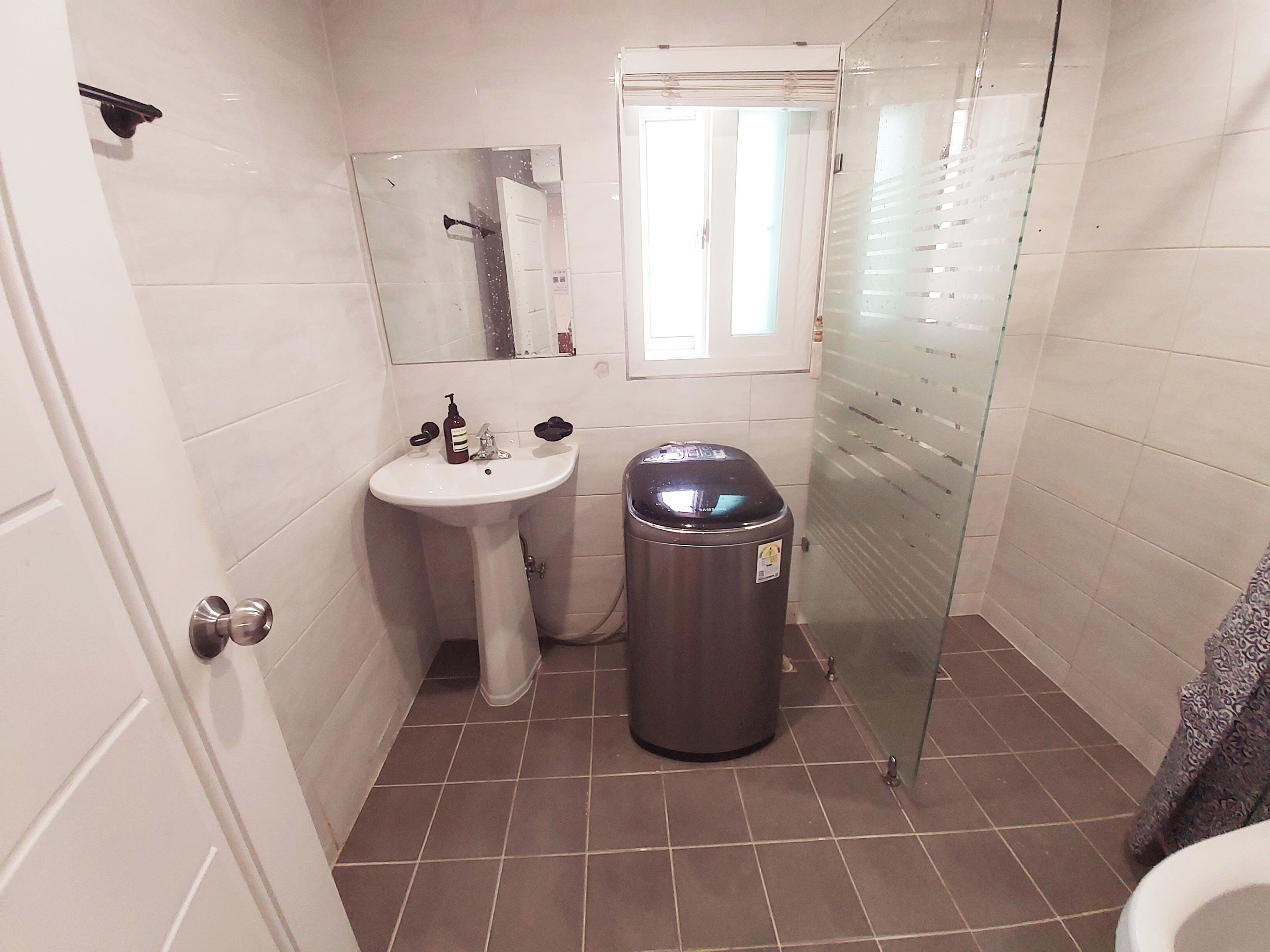 A bathroom with a white sink, a mirror, a trash bin, and a toilet.