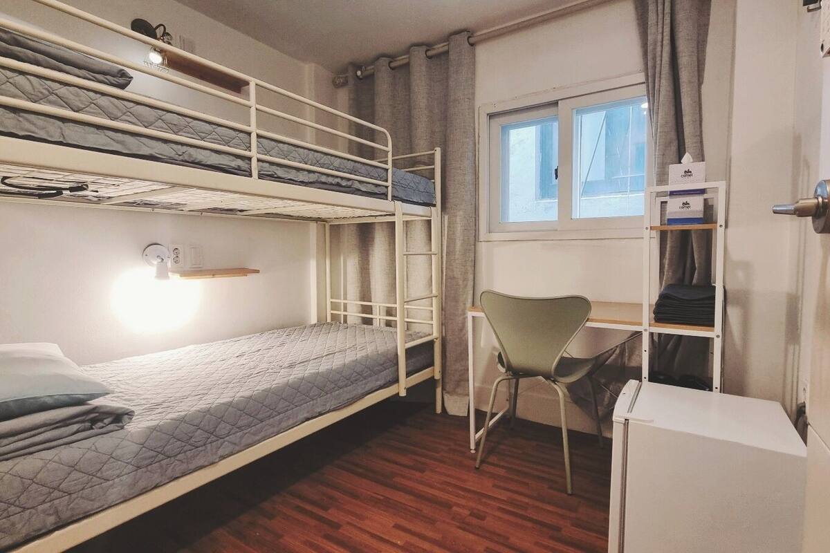 A bunk bed room with a desk and chair, a window, and a door.