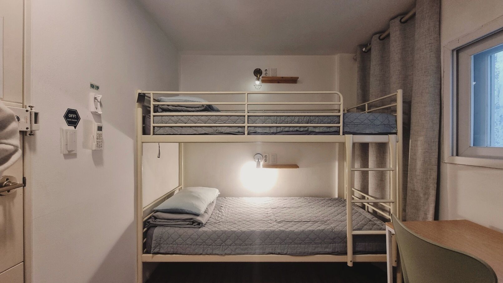 Habitación con literas, un escritorio, una silla, una ventana y una puerta con cerradura y llave.