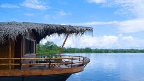 A boat with a thatched roof and wooden deck, docked on calm water with a forested shoreline in the background. - Yathra Houseboat (Bentota)