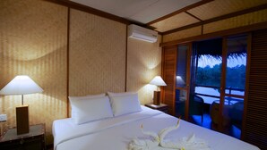 A hotel room with a bed, two bedside lamps, a nightstand, and a window with a view of trees. - Yathra Houseboat (Bentota)