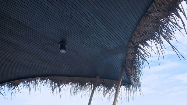 A dining area with a table set for two, a thatched roof, and a view of a calm lake. - Yathra Houseboat (Bentota)