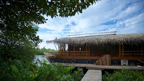 A thatched-roof boat house with a wooden deck and a view of the water. - Yathra Houseboat (Bentota)
