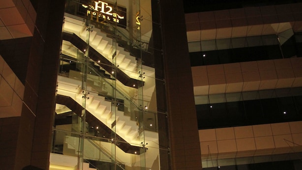 Um hotel moderno com fachada de vidro, vários andares e uma escadaria imponente.