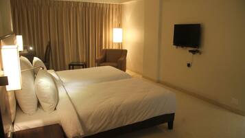 A hotel room with two beds, a chair, a TV, and a lamp.