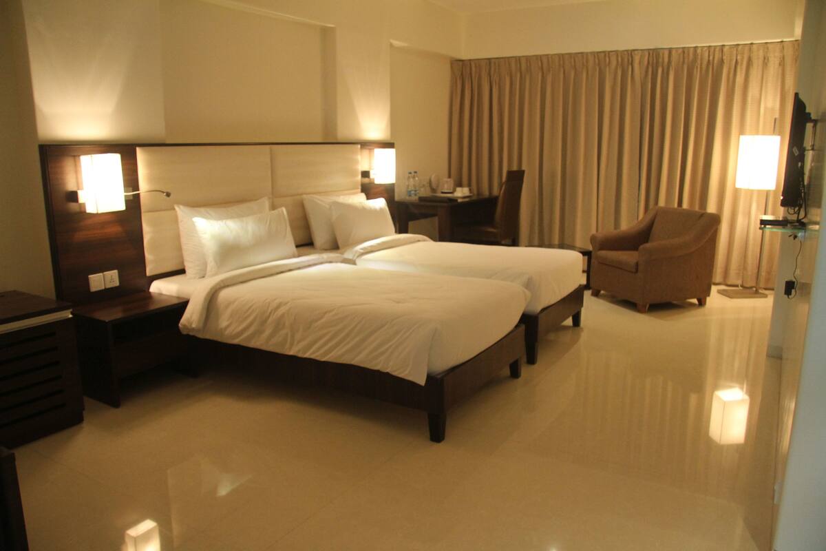 A hotel room with two beds, a desk, a chair, and a TV.