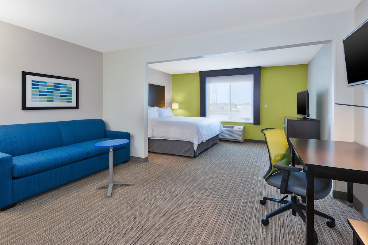 A hotel room with a bed, a blue sofa, a small table, a TV, and a large window.