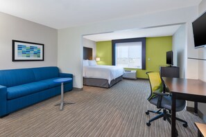 A hotel room with a bed, a blue sofa, a small table, a TV, and a large window. - Holiday Inn Express & Suites Effingham by IHG (Effingham)