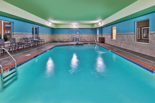 Una piscina interior con agua cristalina, rodeada de sillones de descanso y un suelo de baldosas.
