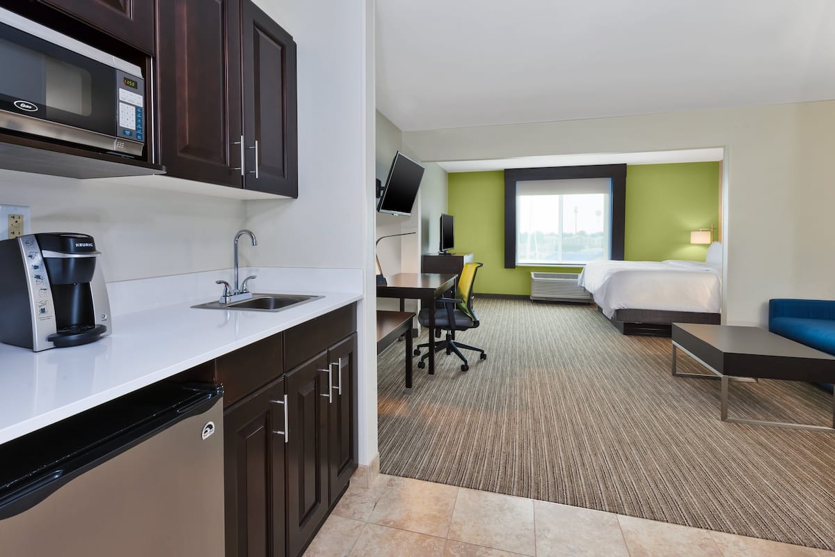 A hotel room with a kitchenette, a bed, a desk, and a TV.